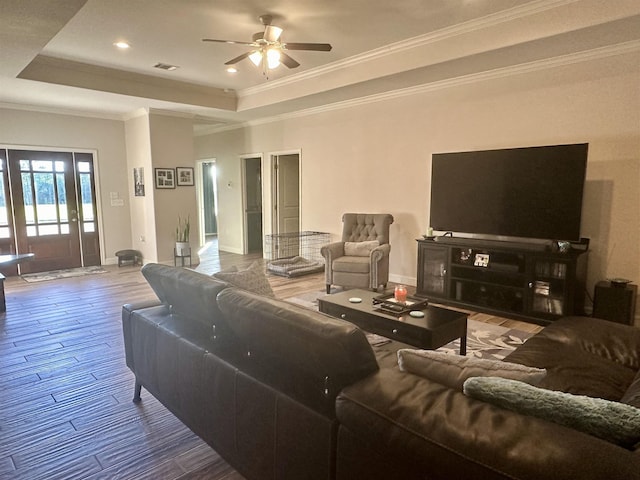 living room with a raised ceiling, ceiling fan, and crown molding