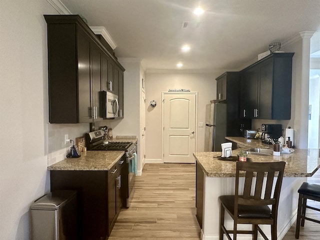 kitchen with light stone countertops, a kitchen breakfast bar, light wood-type flooring, and stainless steel appliances