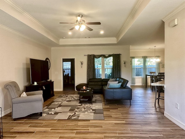 living room with a tray ceiling, crown molding, hardwood / wood-style floors, and ceiling fan with notable chandelier