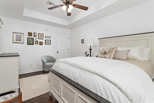 bedroom featuring ceiling fan, dark wood-type flooring, and a tray ceiling