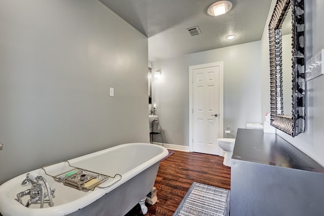 bathroom featuring a textured ceiling, a tub to relax in, toilet, and hardwood / wood-style flooring