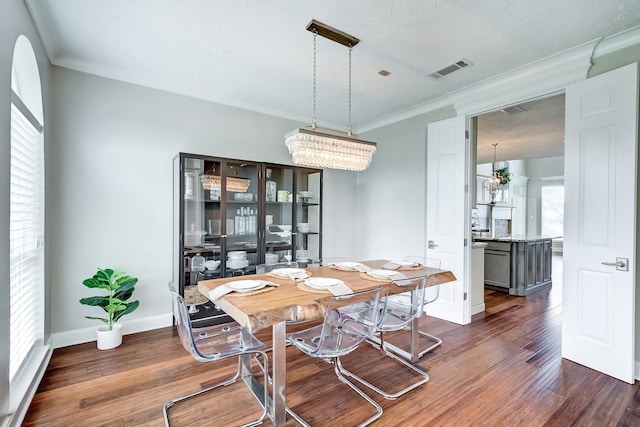 dining space featuring a textured ceiling, dark wood-type flooring, crown molding, and a notable chandelier