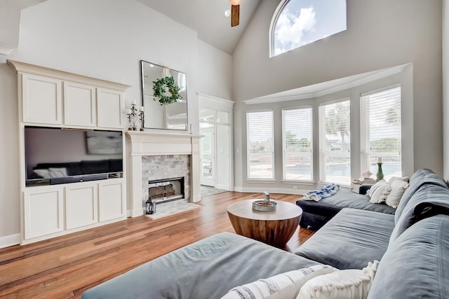 living room with a tiled fireplace, ceiling fan, high vaulted ceiling, and light wood-type flooring