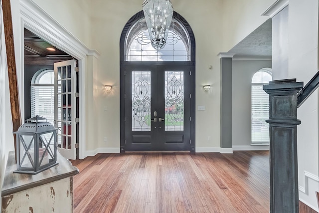 entrance foyer with french doors, ornamental molding, wood-type flooring, a chandelier, and a high ceiling