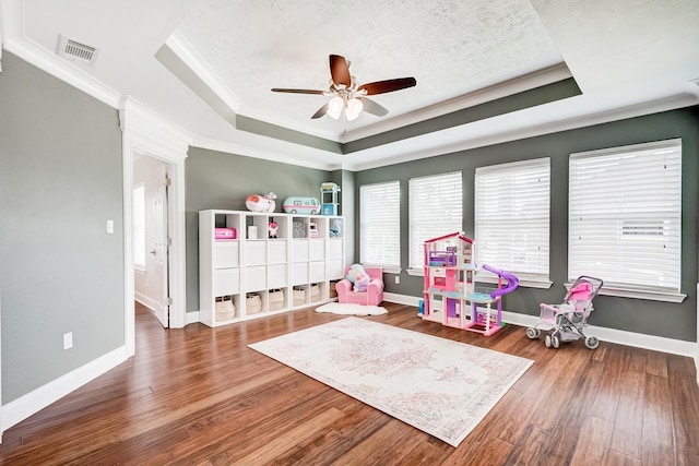 recreation room with a raised ceiling, ceiling fan, wood-type flooring, and ornamental molding