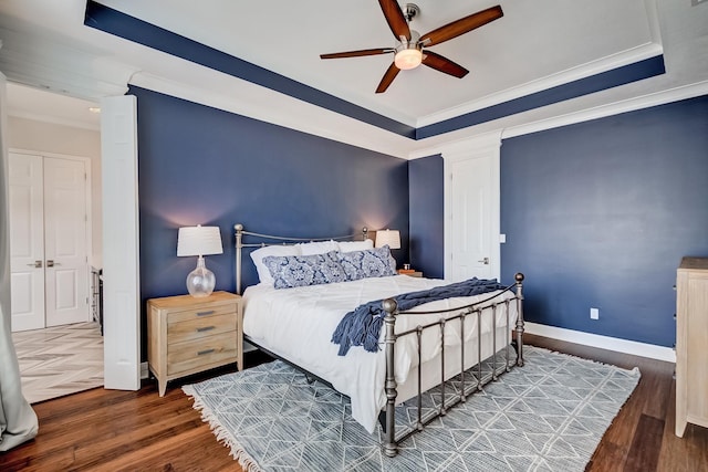 bedroom featuring dark wood-type flooring, ceiling fan, ornamental molding, and a tray ceiling