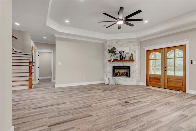 unfurnished living room with ceiling fan, light wood-type flooring, a tray ceiling, and french doors