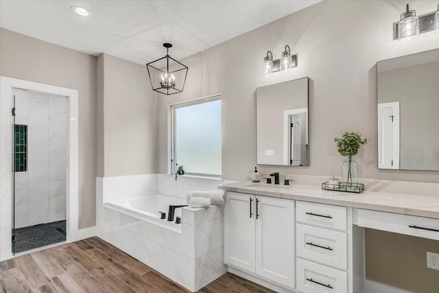 bathroom with wood-type flooring, vanity, an inviting chandelier, and separate shower and tub