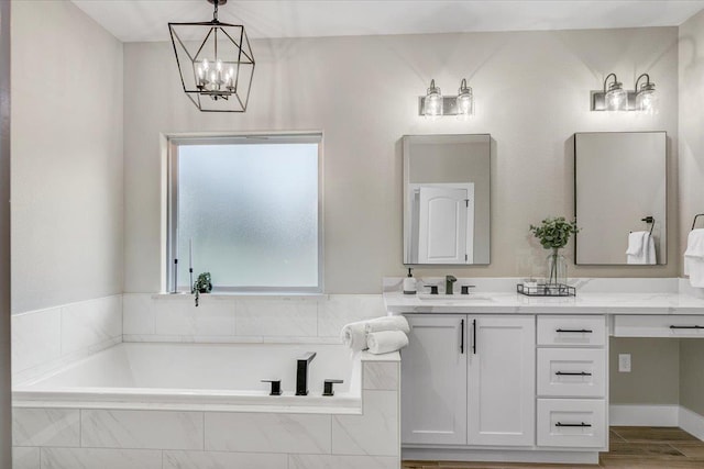 bathroom featuring vanity, a relaxing tiled tub, and an inviting chandelier