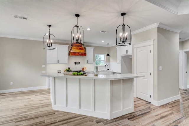 kitchen with white cabinets, decorative light fixtures, sink, and an island with sink