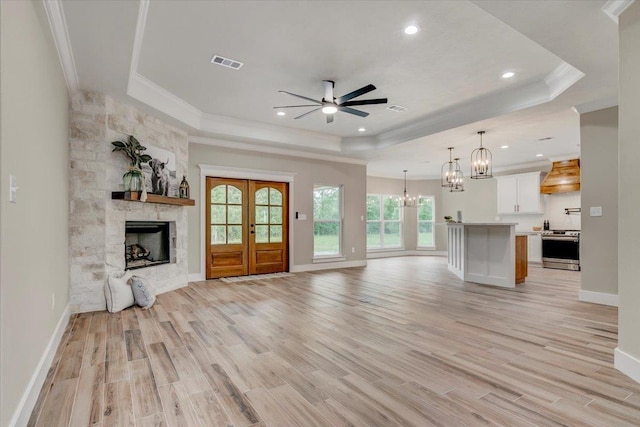 unfurnished living room featuring ceiling fan with notable chandelier, a tray ceiling, and a wealth of natural light