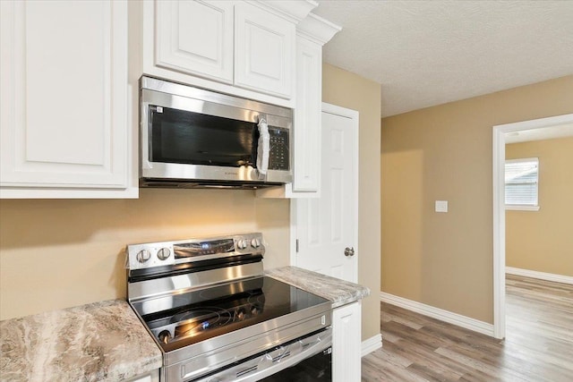 kitchen with a textured ceiling, light stone counters, white cabinetry, and stainless steel appliances