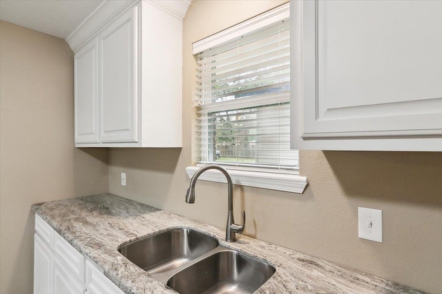 kitchen with light stone countertops, sink, and white cabinets