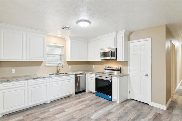 kitchen featuring white cabinets, sink, light hardwood / wood-style flooring, a textured ceiling, and stainless steel appliances