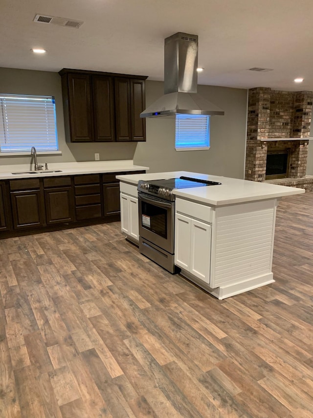 kitchen with island exhaust hood, a sink, wood finished floors, light countertops, and stainless steel electric range oven