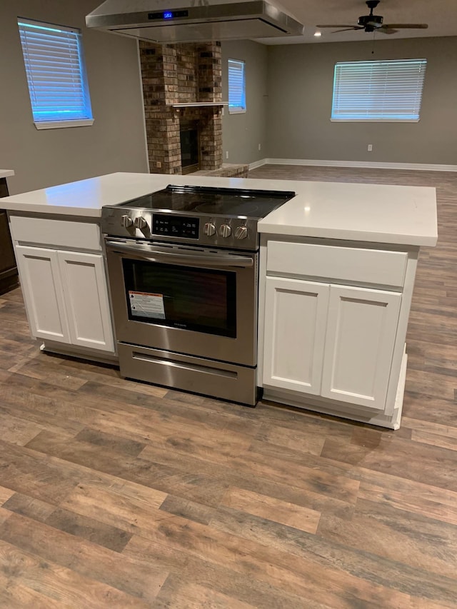 kitchen with stainless steel electric range oven, open floor plan, exhaust hood, and white cabinetry