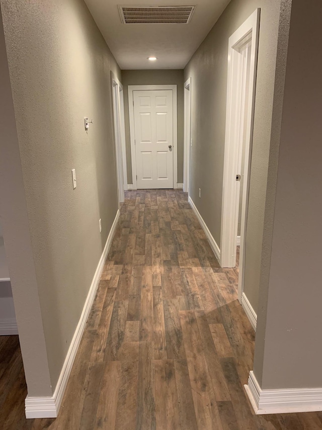 hallway featuring visible vents, baseboards, and dark wood-style flooring