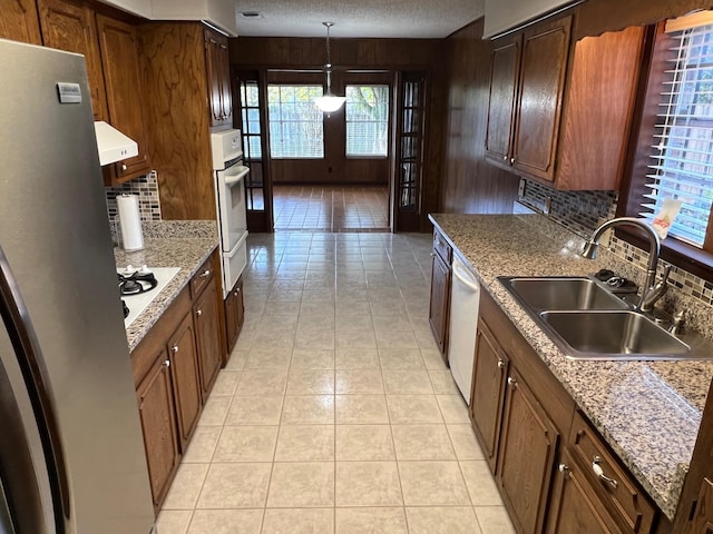 kitchen featuring sink, range hood, backsplash, decorative light fixtures, and white appliances