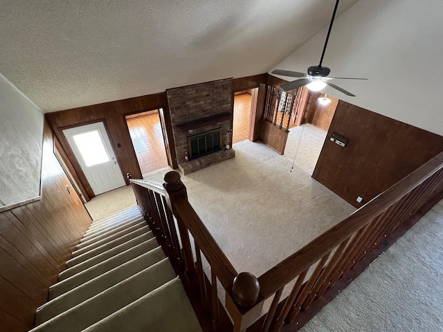 stairs with a fireplace, a textured ceiling, ceiling fan, and wooden walls