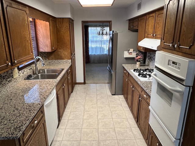 kitchen featuring sink, an inviting chandelier, dark stone counters, white appliances, and exhaust hood