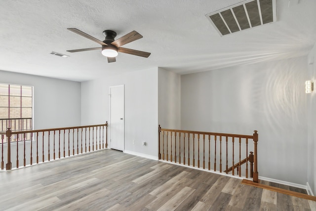 empty room featuring a textured ceiling, light wood-type flooring, and ceiling fan