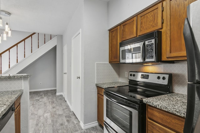 kitchen featuring stainless steel appliances, tasteful backsplash, decorative light fixtures, stone countertops, and light wood-type flooring