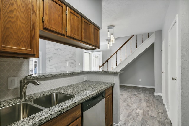 kitchen with light stone countertops, dishwasher, sink, decorative light fixtures, and decorative backsplash