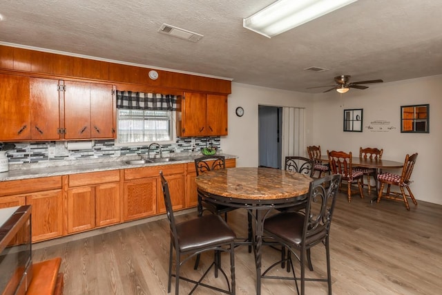 kitchen with light wood finished floors, visible vents, decorative backsplash, brown cabinets, and a sink