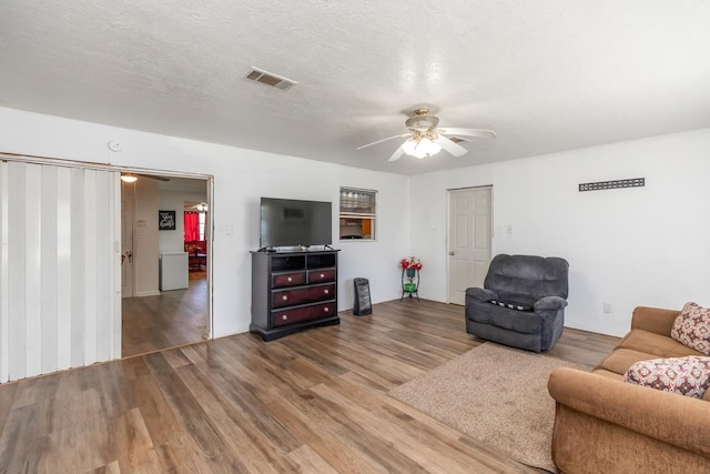 living area featuring a textured ceiling, wood finished floors, visible vents, and a ceiling fan