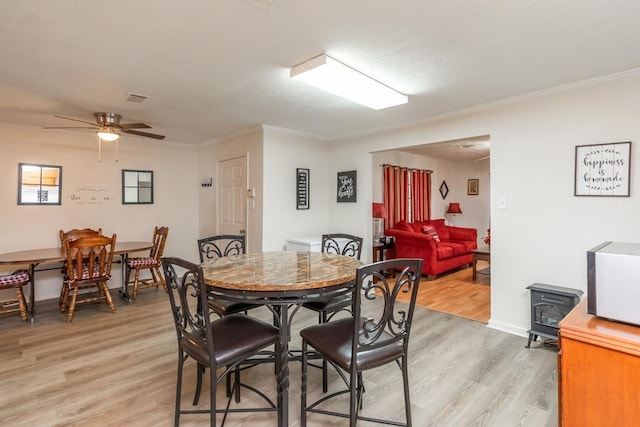 dining room with a wood stove, crown molding, light wood finished floors, and ceiling fan