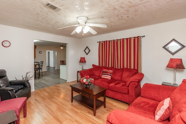 living area with visible vents, ceiling fan, light wood-style flooring, and a textured ceiling