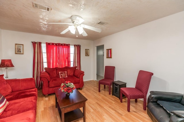 living area with light wood finished floors, a textured ceiling, visible vents, and a ceiling fan