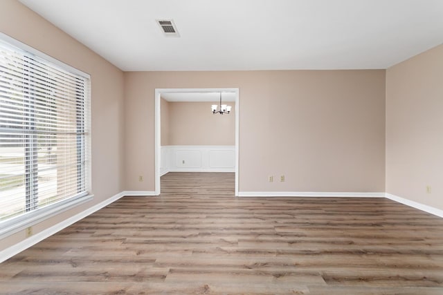 unfurnished room with baseboards, visible vents, an inviting chandelier, and wood finished floors