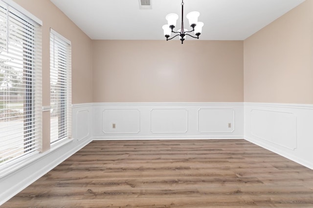 spare room featuring a chandelier, wainscoting, visible vents, and wood finished floors