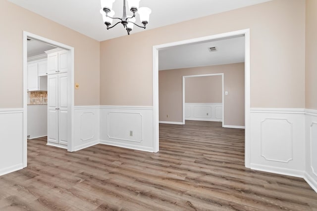 unfurnished dining area with a chandelier, wainscoting, visible vents, and light wood-style floors