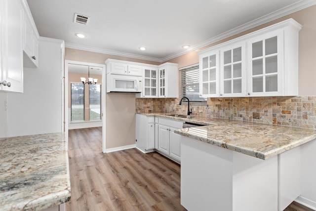 kitchen with visible vents, white cabinets, ornamental molding, a peninsula, and a sink