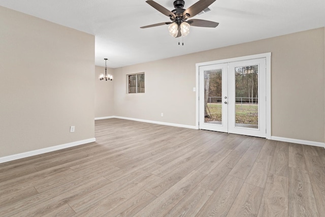 spare room featuring ceiling fan with notable chandelier, light hardwood / wood-style floors, and french doors