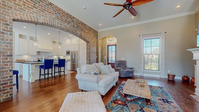 living area featuring arched walkways, brick wall, dark wood-style flooring, crown molding, and a fireplace