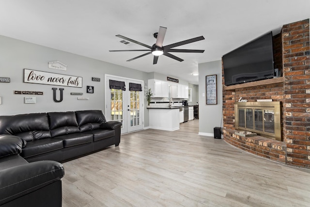 living area featuring a fireplace, visible vents, a ceiling fan, french doors, and light wood-type flooring