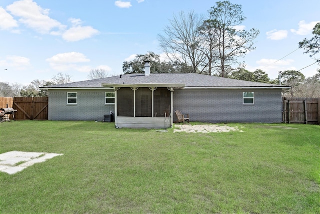 rear view of house with brick siding, a yard, a chimney, a sunroom, and fence