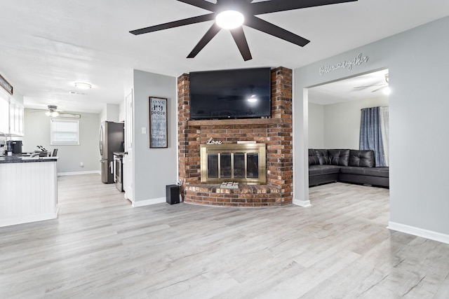 unfurnished living room featuring light wood finished floors, a fireplace, baseboards, and a ceiling fan