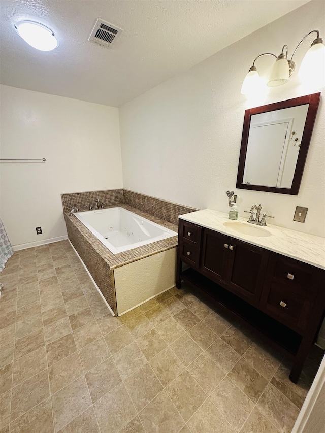 bathroom with a textured ceiling, vanity, and a relaxing tiled tub