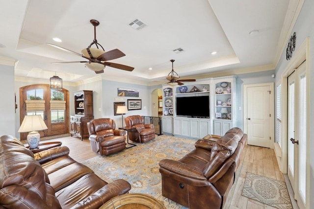 living area with arched walkways, a raised ceiling, visible vents, and light wood-style floors