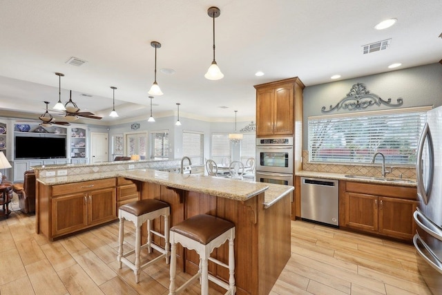 kitchen with appliances with stainless steel finishes, a large island with sink, brown cabinets, and a sink