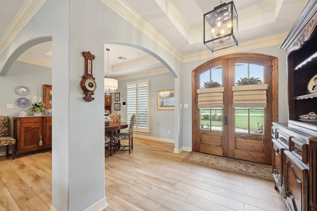 entrance foyer with arched walkways, a raised ceiling, light wood finished floors, and french doors