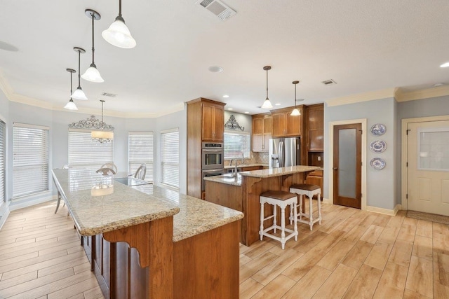 kitchen with crown molding, visible vents, light wood-style flooring, appliances with stainless steel finishes, and a kitchen island with sink