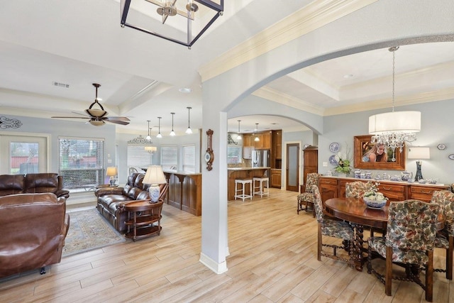 living room with arched walkways, visible vents, light wood-style floors, ornamental molding, and a tray ceiling