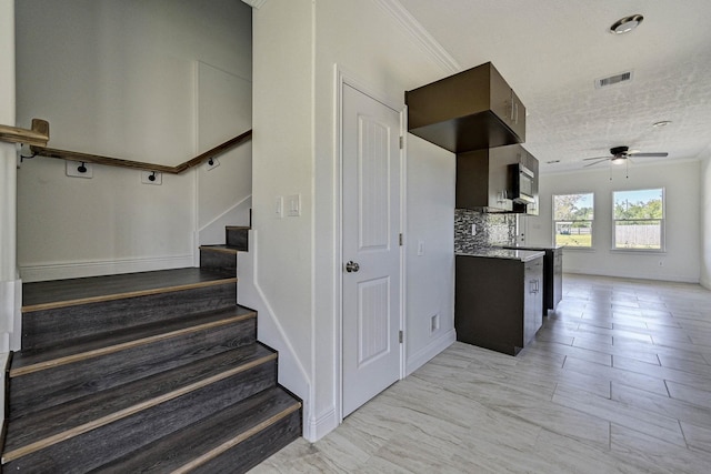 stairs with a textured ceiling, ceiling fan, and crown molding