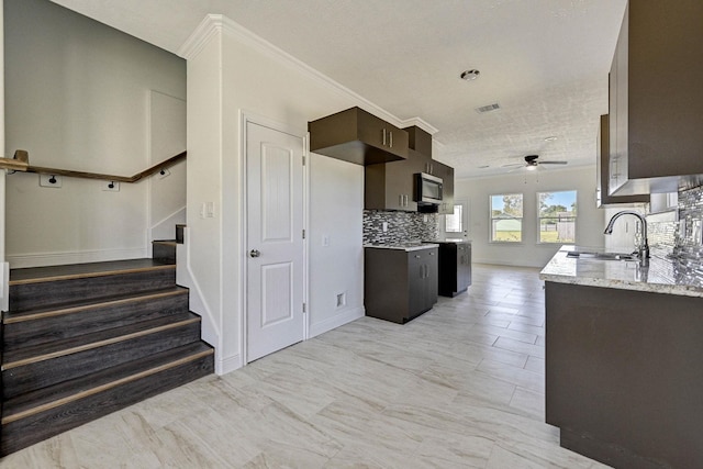 kitchen featuring dark brown cabinetry, ceiling fan, sink, light stone counters, and decorative backsplash