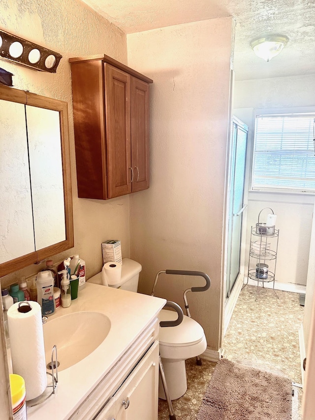 bathroom featuring vanity, toilet, a shower with shower door, and a textured ceiling